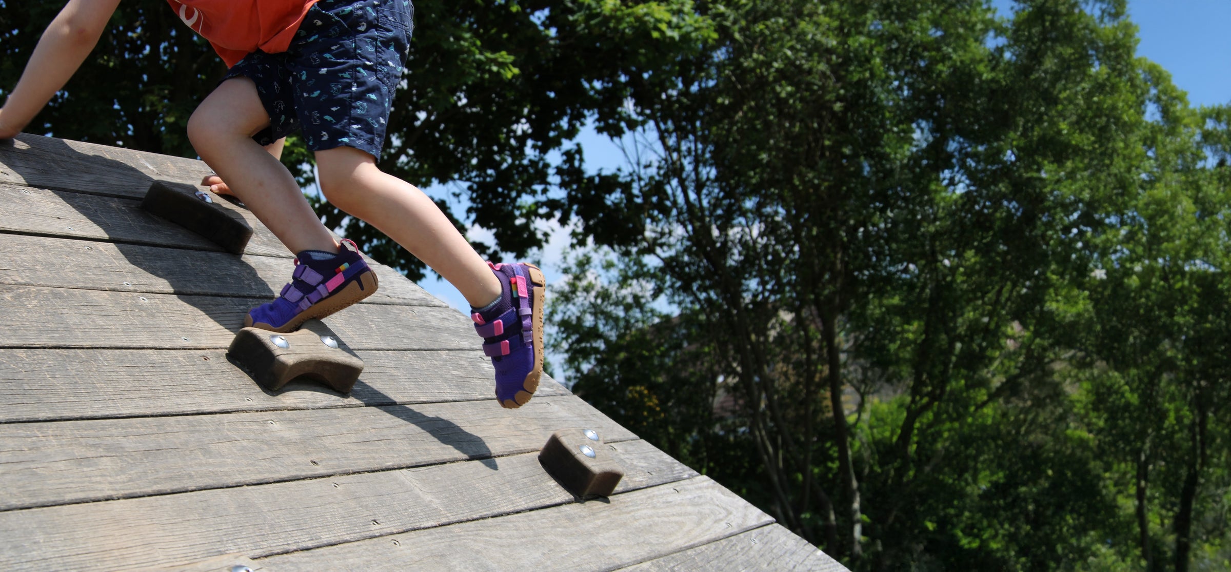 Kind klettert mit Sizeless Kinderschuhen auf dem Spielplatz und bewegt sich natürlich im Freien